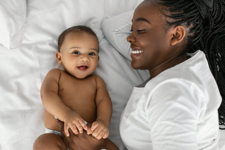 African American mom lying in bed with her laughing baby