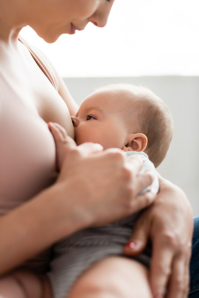 selective focus of caring mother breastfeeding baby boy in bedroom