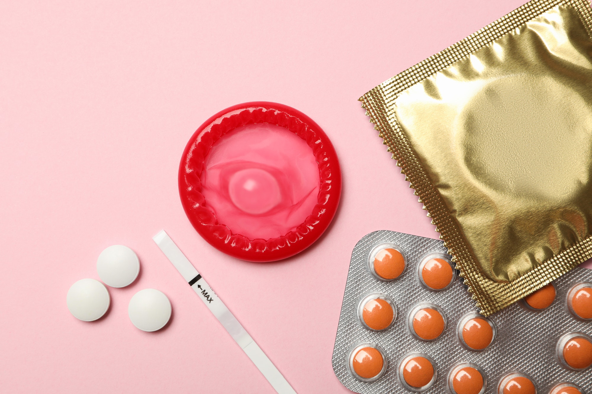 Condoms and pills on pink background, top view