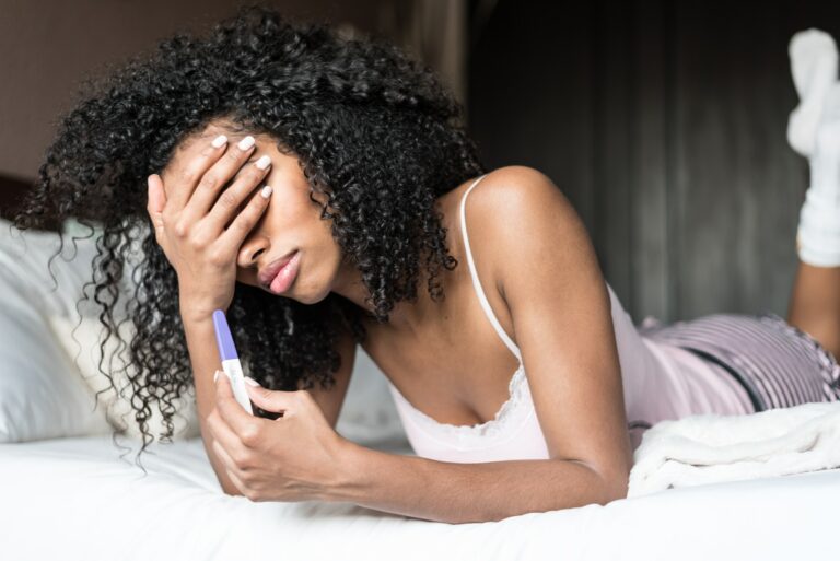 sad and worried woman with a pregnancy test on bed