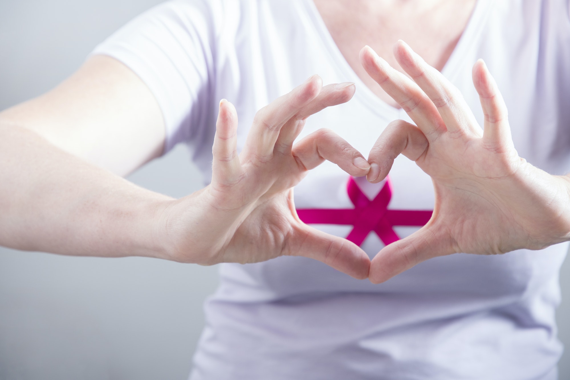 woman making heart sign with fingers on breast cancer protection symbol background