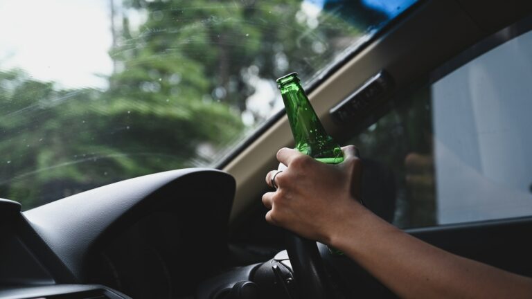 Man driving a car and holding bottle of beer. Don't drink and drive concept.